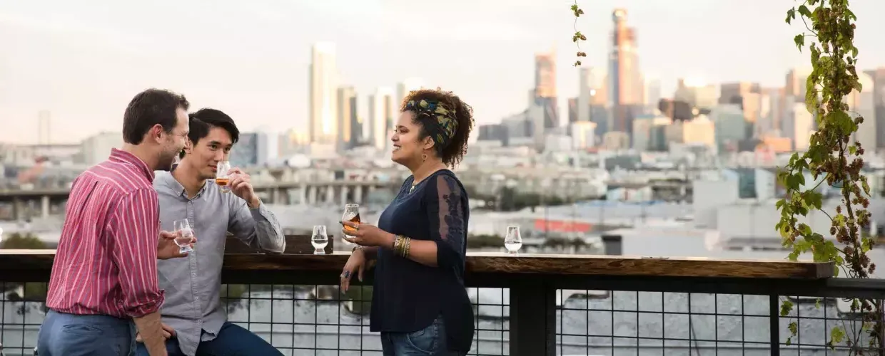 Three people gather around an outdoor table on the roof deck of Anchor Distilling in San Francisco, California.